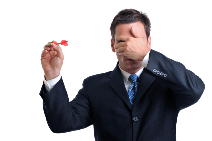 A man covering his eyes while trying to throw a dart.