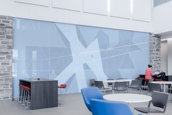 Clean open-concept lobby with geometric vinyl wrapped wall and with blue and grey chairs and white table featured in bottom right corner