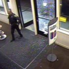 A police officer entering a store after the store front glass had been shattered.
