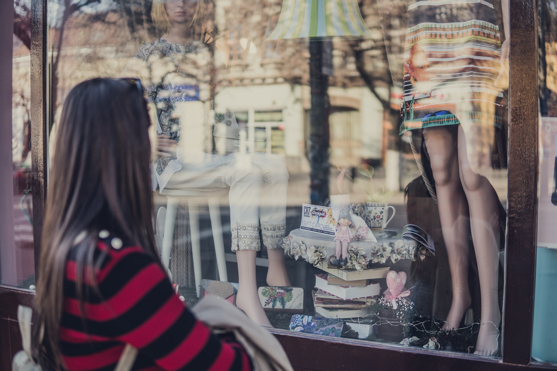 A girl looking in a window at a mannequin and clothes